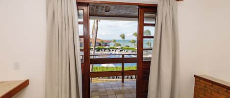 A room with a bed, a wooden headboard, a view of a pool and palm trees through a glass door.