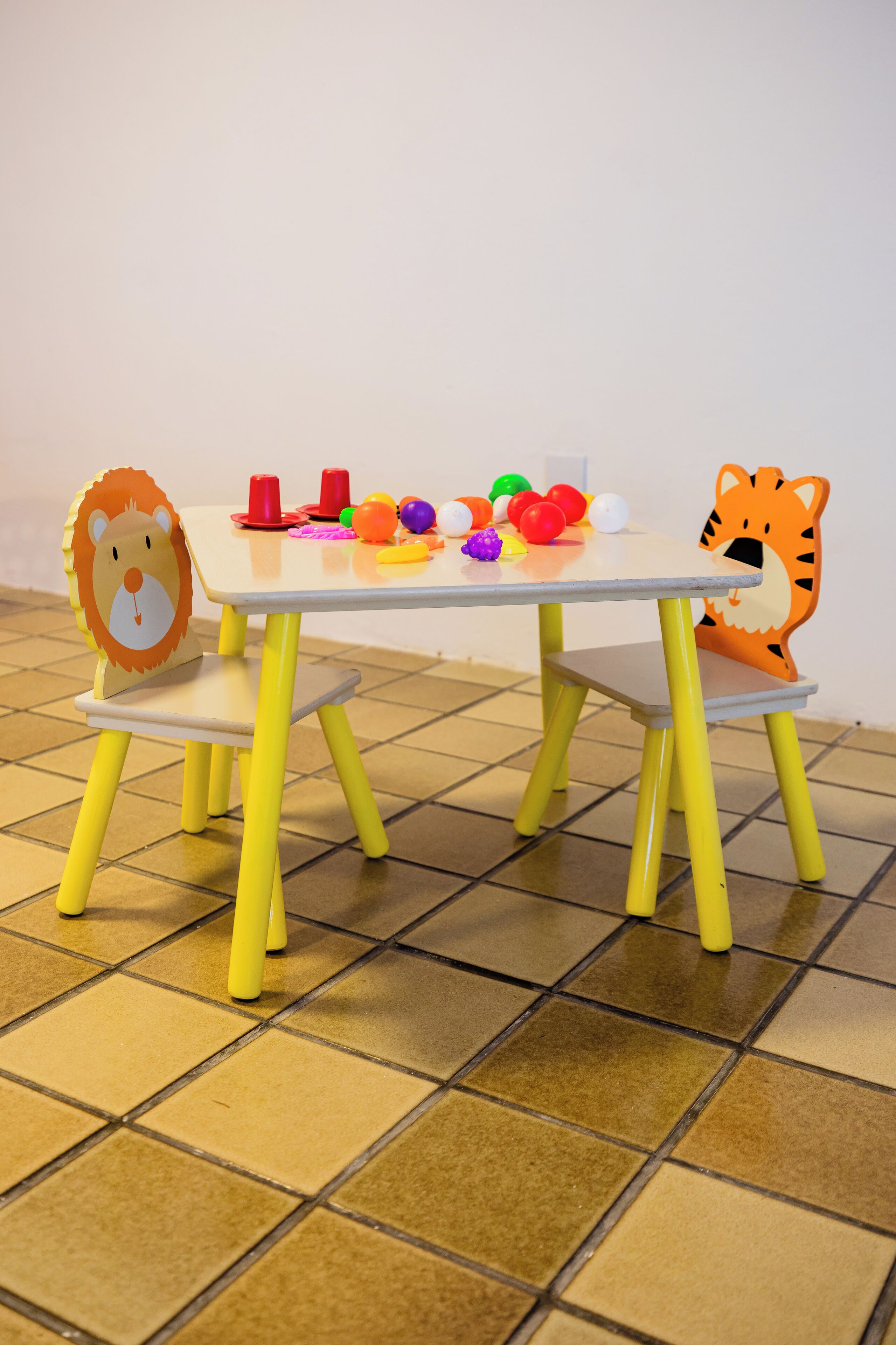 A small table with a lion and tiger chair design, a white tabletop, and colorful toys on the table.