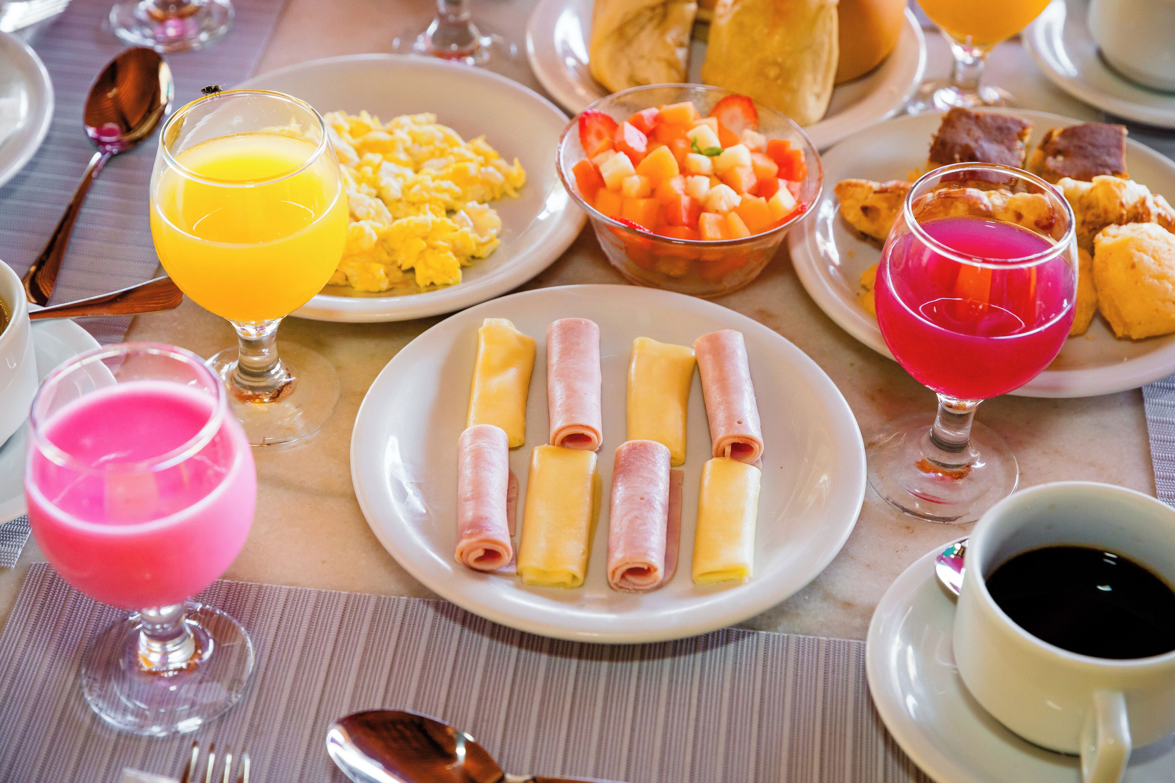 Een ontbijtsetting met borden roerei, fruit, hamrolletjes en diverse drankjes.