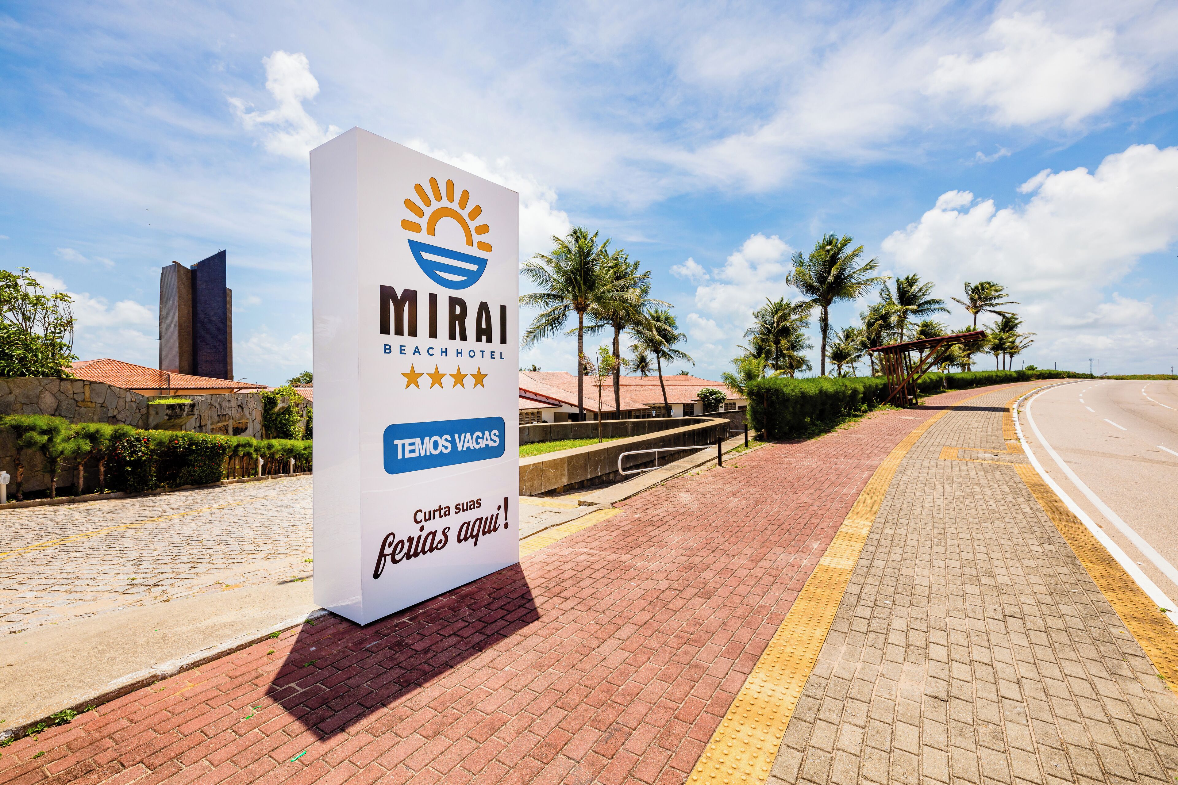Naamplaatje voor Mirai Beach Hotel, met een heldere lucht en palmbomen op de achtergrond.