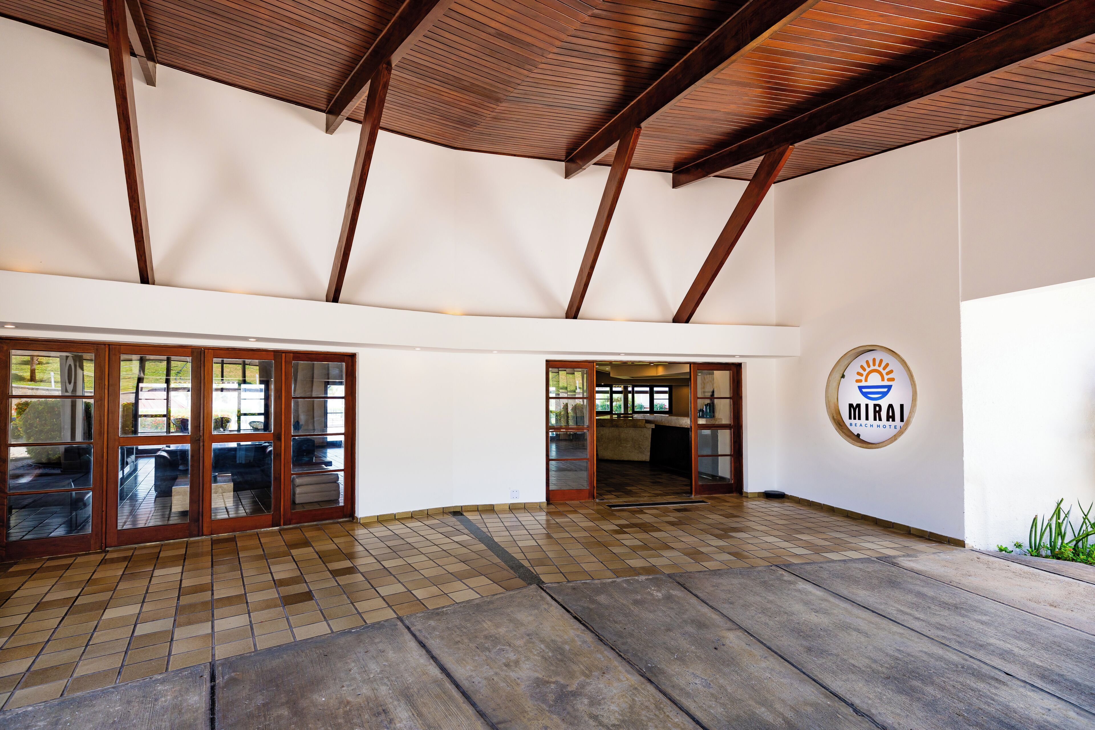 A spacious indoor area with a tiled floor, wooden ceiling beams, and glass doors leading to an outdoor area.