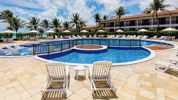 A pool area with lounge chairs, a small table, and a building with a red roof in the background.