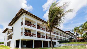 Un hotel de varios pisos con fachada blanca, balcones de madera y una palmera en primer plano.