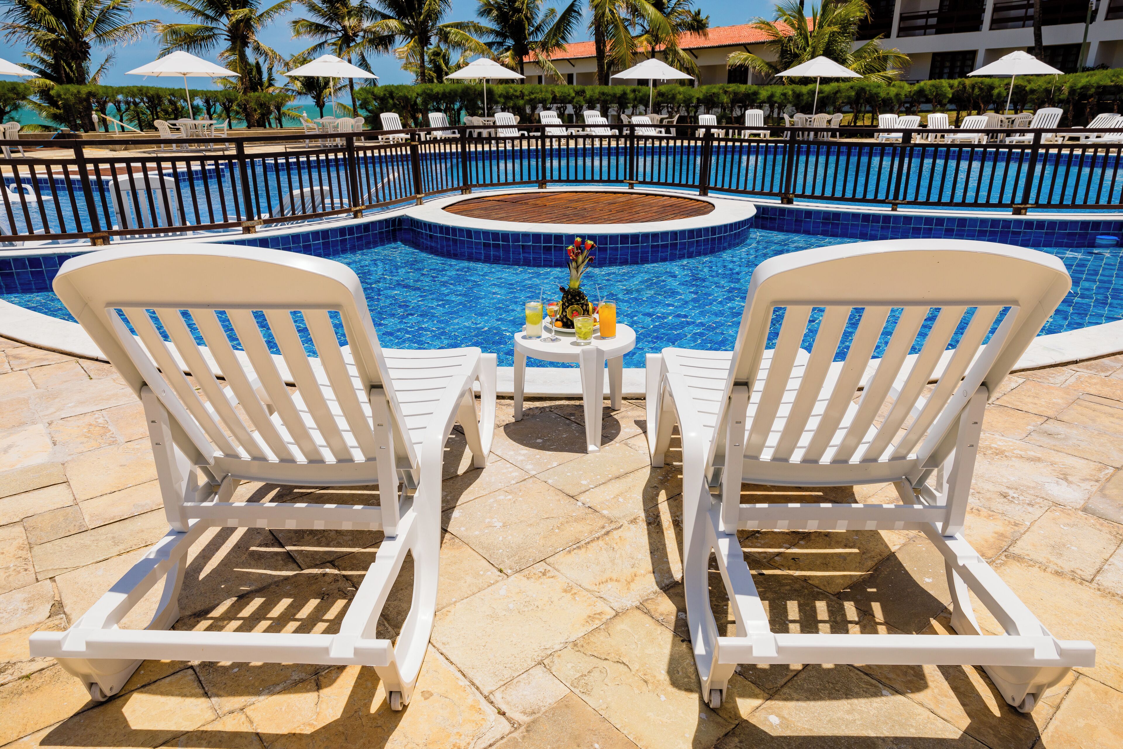 A poolside area with two white lounge chairs, a small table with drinks, and a pool with a blue tile border.