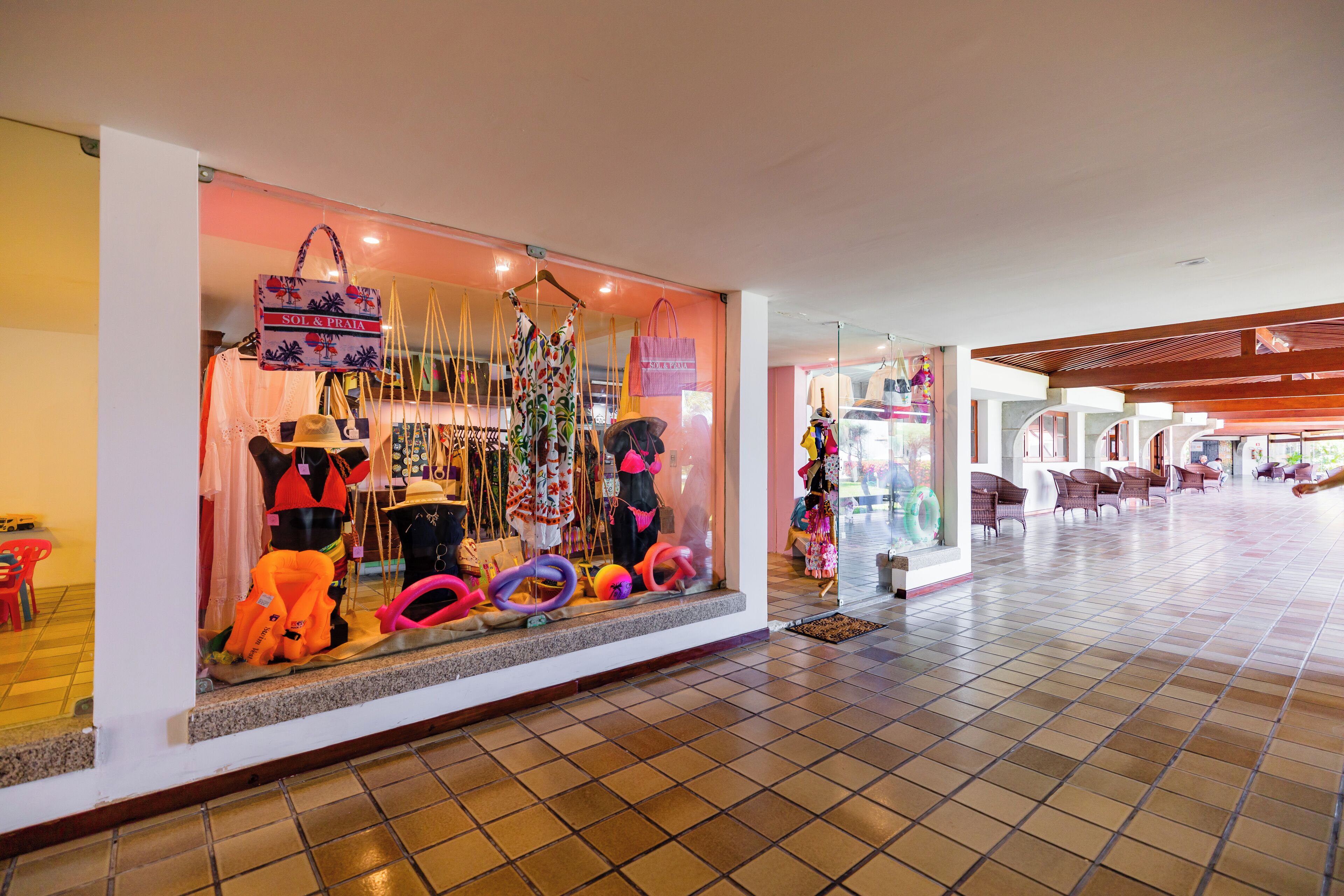 A hotel lobby with a tiled floor, a seating area with chairs, and a storefront with colorful items on display.