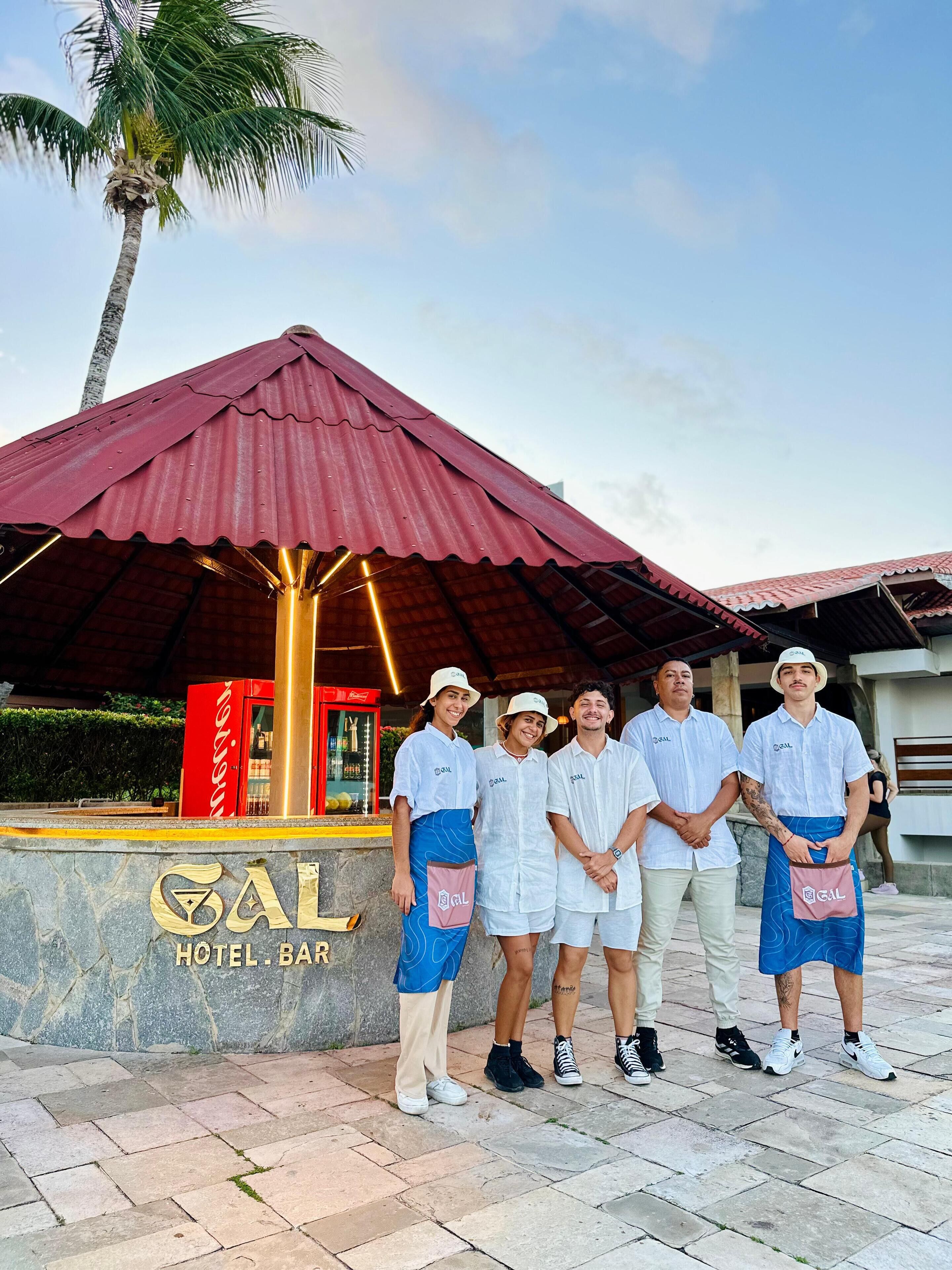 A group of people standing in front of a hotel bar with a red roof and a sign that reads "GAL HOTEL BAR".