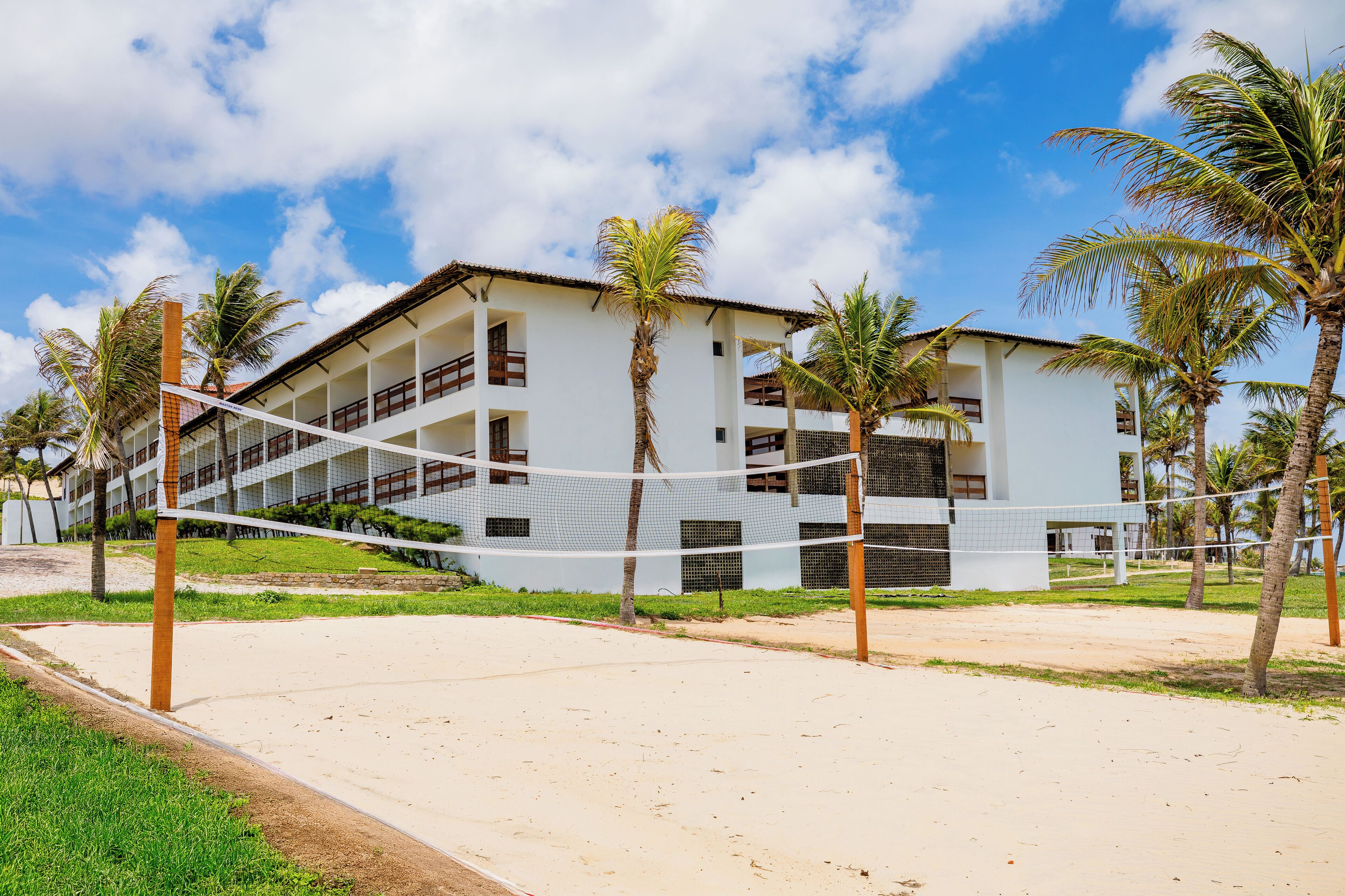 Un hotel frente a la playa con fachada blanca, varios balcones y palmeras.