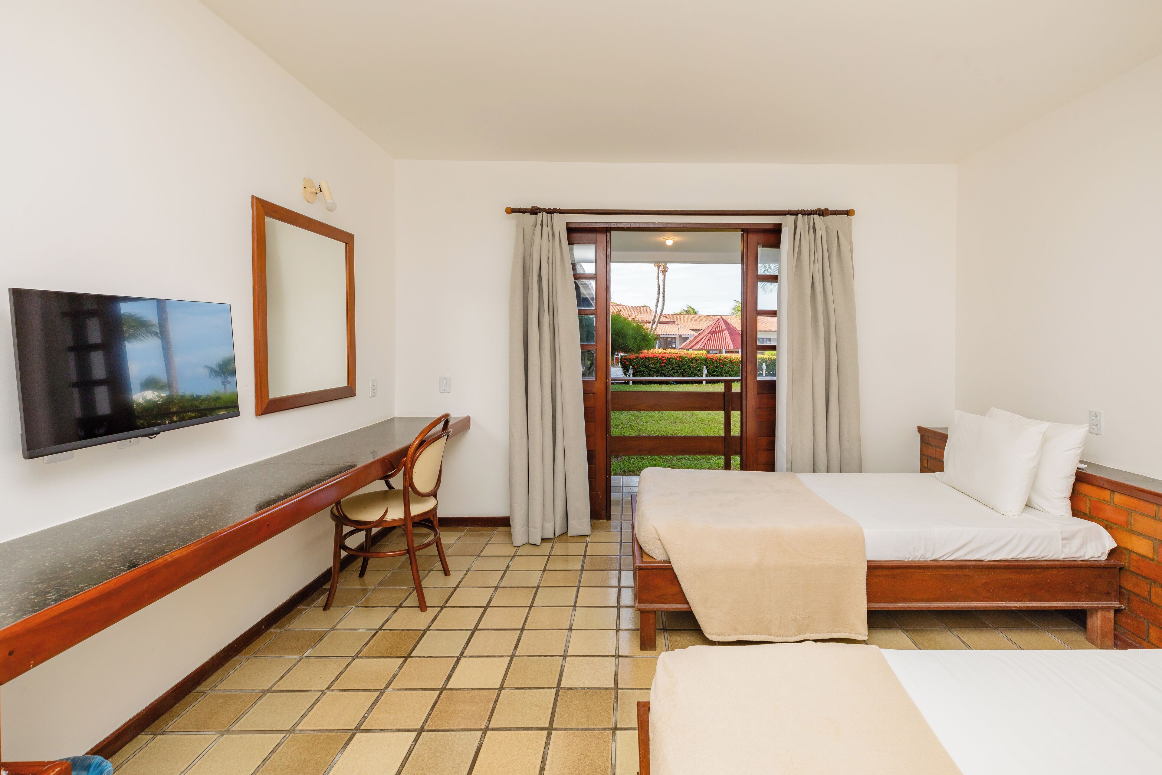 A hotel room with two beds, a desk, a chair, a TV, and a view of the outside.