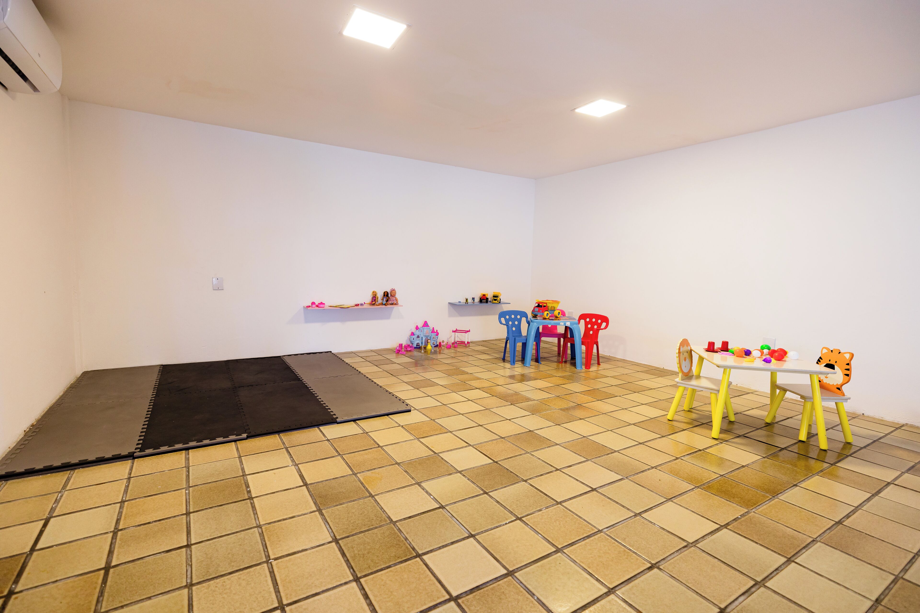 Een kamer met een betegelde vloer, een zwarte mat, een witte tafel met stoelen en planken met speelgoed.