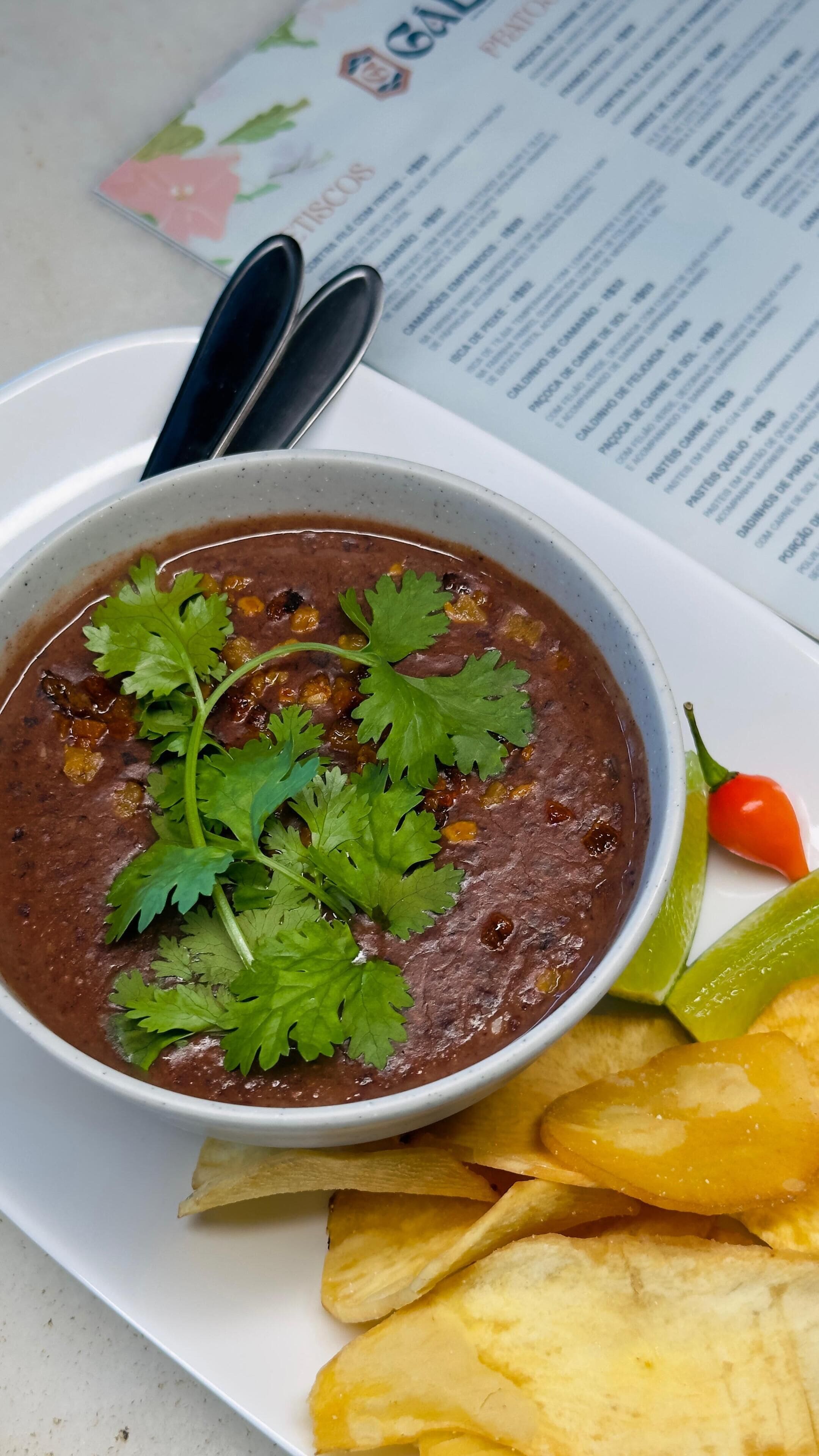 En skål sortbønnesuppe pyntet med koriander, serveret med tortilla chips og en limeskive.
