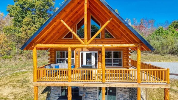 A log cabin with a balcony, stone foundation, and a steeply pitched roof.