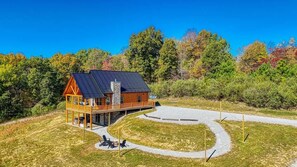 A log cabin with a porch, a stone chimney, and a paved driveway.