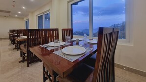 Comedor con mesas y sillas de madera, ventanas amplias con vistas a montañas y un diseño moderno de techo.