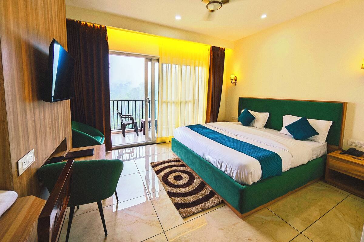 Habitación de hotel con cama, escritorio, silla, televisor y balcón con vistas.