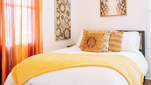 A bedroom with a wooden bed, white bedding, a yellow throw blanket, and two wall art pieces. - “La Playa” Downtown Brunswick Beach Cottage - near St. Simons & Jekyll  (Brunswick)