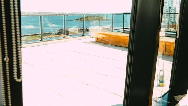 A view through a window of a balcony with a clear sky and a distant body of water.