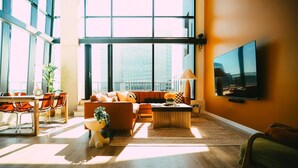 A modern living room with a large window, a sofa, a coffee table, and a TV mounted on the wall.
