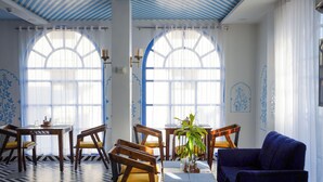 A dining area with wooden chairs and tables, large arched windows, and a blue sofa.