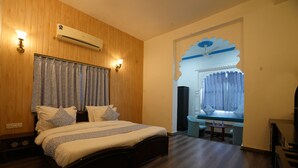 A bedroom with a wooden headboard, a bed with patterned bedding, a small table, and a window with curtains.