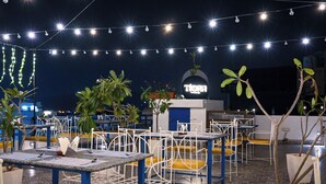 An outdoor seating area with tables and chairs, string lights, and potted plants.