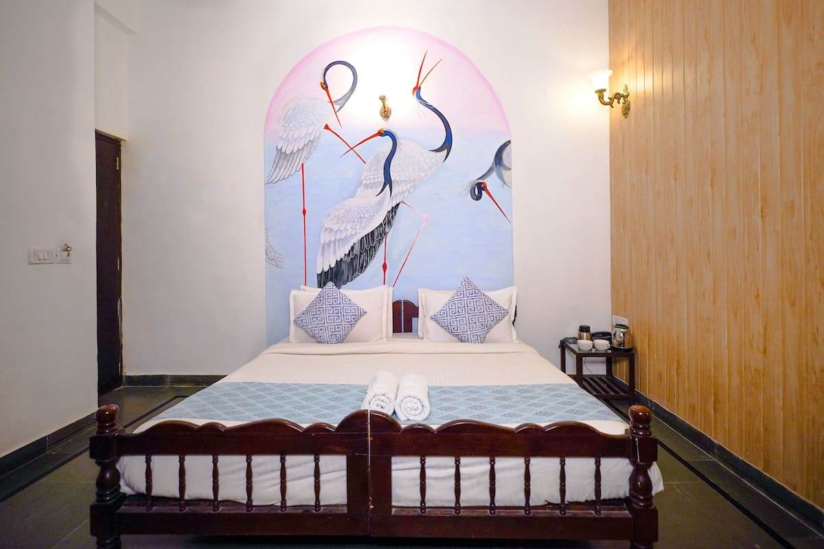 Un lit bien fait, recouvert d’une couvre-lit à motifs bleus et blancs, avec deux oreillers à dessins géométriques et une paire de serviettes enroulées posées sur le lit.