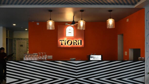 A reception area with a black and white chevron-patterned counter, a sign reading "TIORA" above, and three pendant lights.