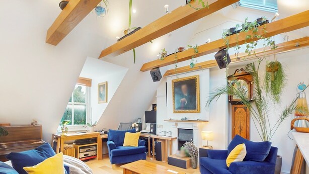 A modern living room with a sloped ceiling, wooden beams, blue sofas, a wooden coffee table, and various plants. - Elegant flat in trendy Hampstead - Pass the Keys (London)