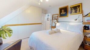 A hotel room with a large bed, a desk, a chair, a plant, and a staircase. - Elegant flat in trendy Hampstead - Pass the Keys (London)