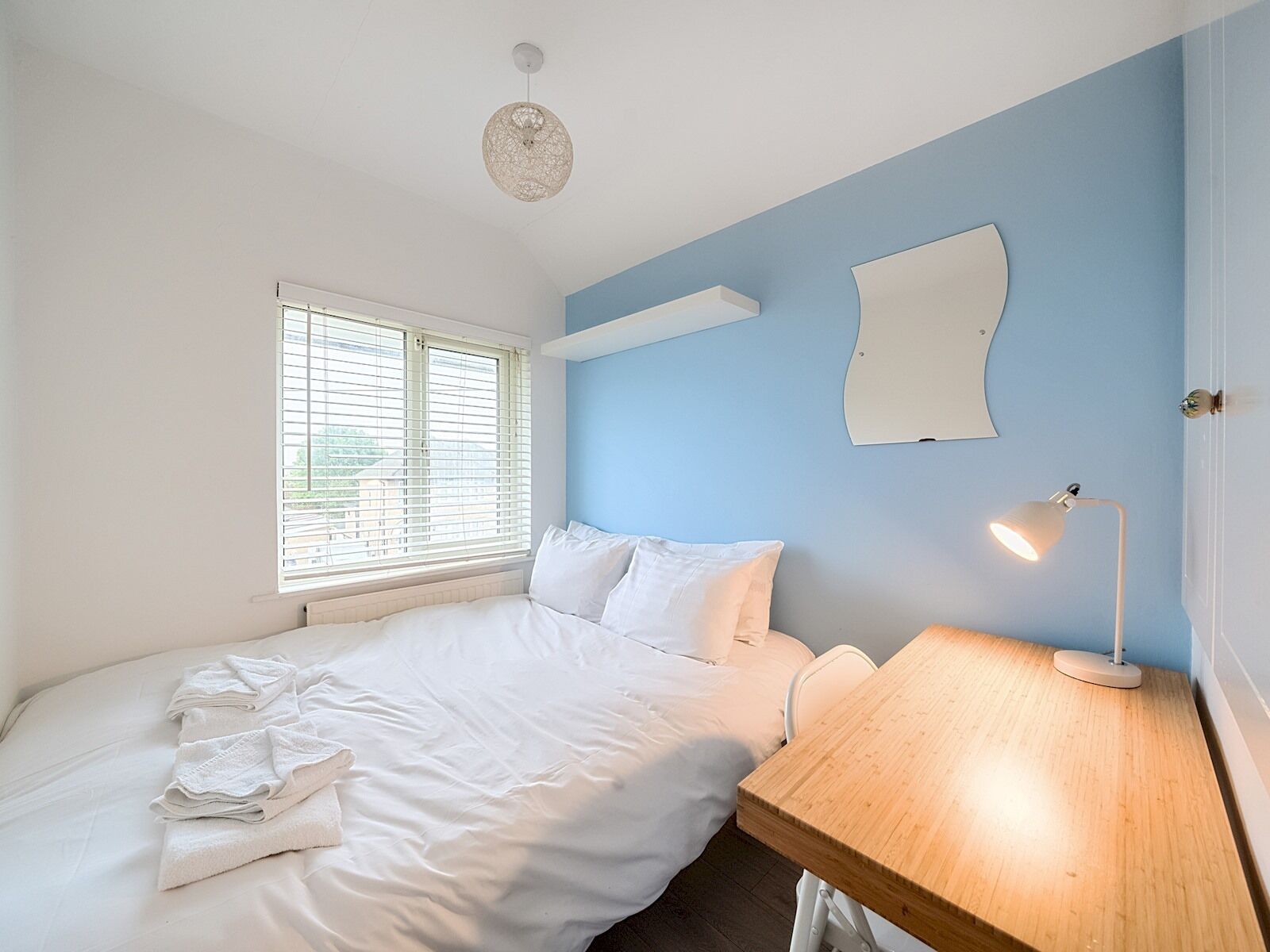 A bedroom with a bed, a desk, a lamp, and a window with blinds.