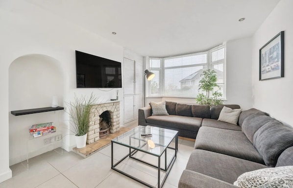 A modern living room with a sofa, a glass coffee table, a fireplace, and a mounted TV.