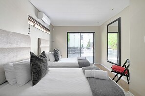Two large beds with white linens and a variety of pillows, including a distinctive patterned one, are featured in this stylish room.
