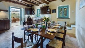 A spacious dining area with a long wooden table set for a meal, surrounded by dark wooden chairs with woven seats. - Casa Pippin 8, Emma Villas (Cortona)