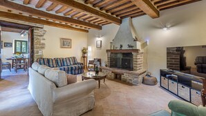 A cozy living room with a fireplace, wooden beams, a sofa, and a television. - Casa Pippin 8, Emma Villas (Cortona)
