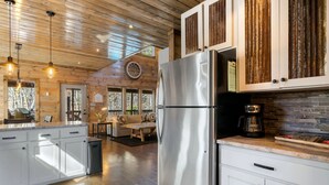 A modern kitchen with a stainless steel refrigerator, wooden cabinets, and a stone backsplash. - SkyHorse Lodge (direct access to national forest) 3 bedroom, 3.5 bath (Broken Bow)