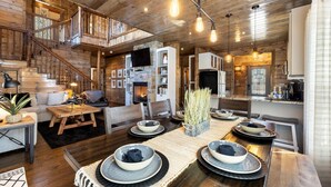 A spacious living area with a wooden staircase, a fireplace, and a dining table set for four. - SkyHorse Lodge (direct access to national forest) 3 bedroom, 3.5 bath (Broken Bow)