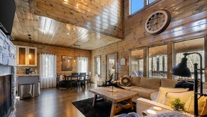 A spacious living room with a fireplace, wooden ceiling, and large windows. - SkyHorse Lodge (direct access to national forest) 3 bedroom, 3.5 bath (Broken Bow)