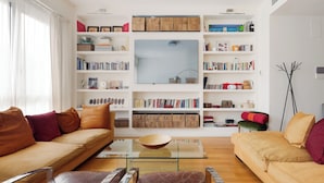 A modern living room with a sofa, armchairs, a coffee table, and a bookshelf filled with books and decorative items. - Brera Apartments in Arena (Milan)