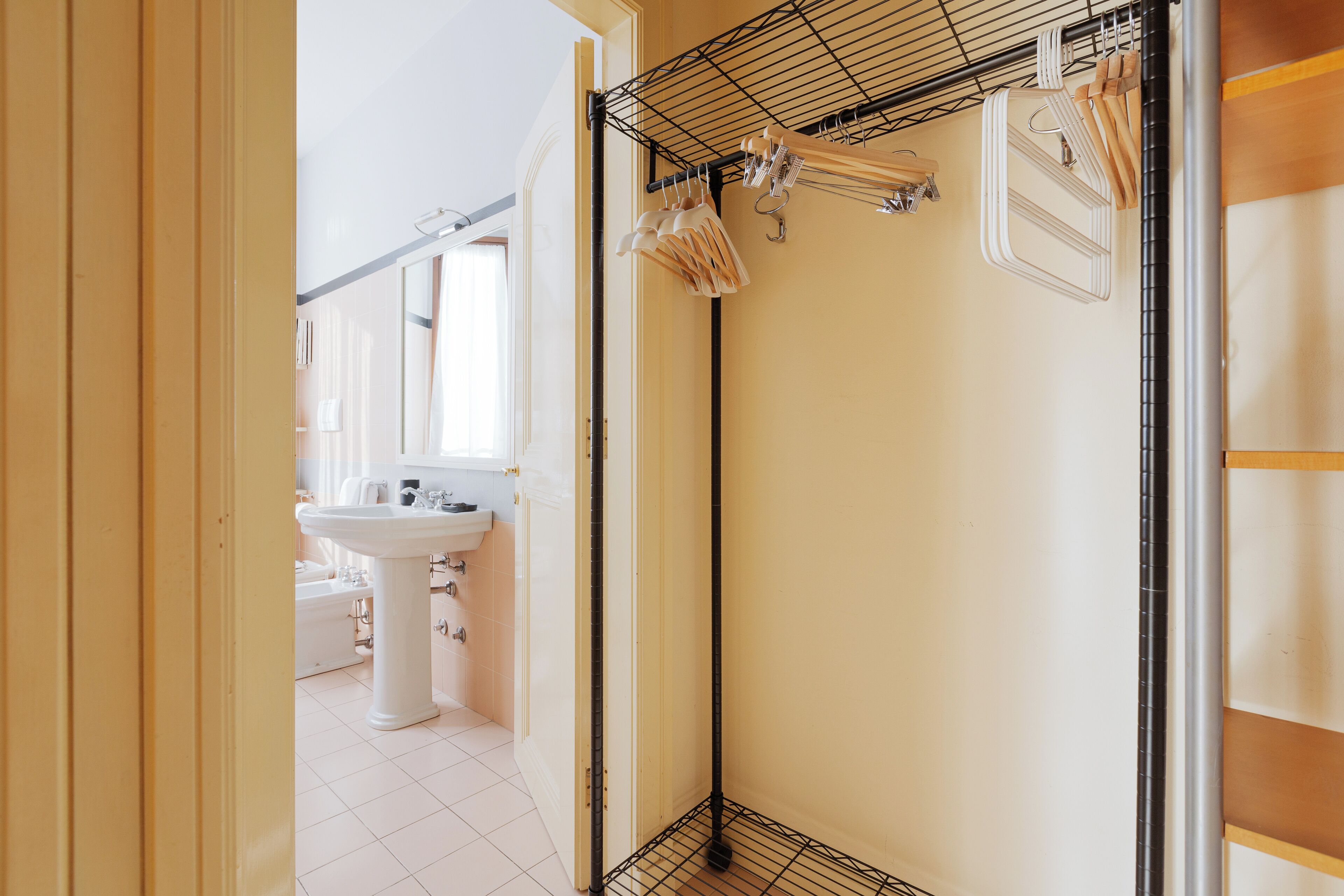 A narrow hallway with a white sink and cabinets, a black metal rack with wooden hangers, and a wooden door frame.