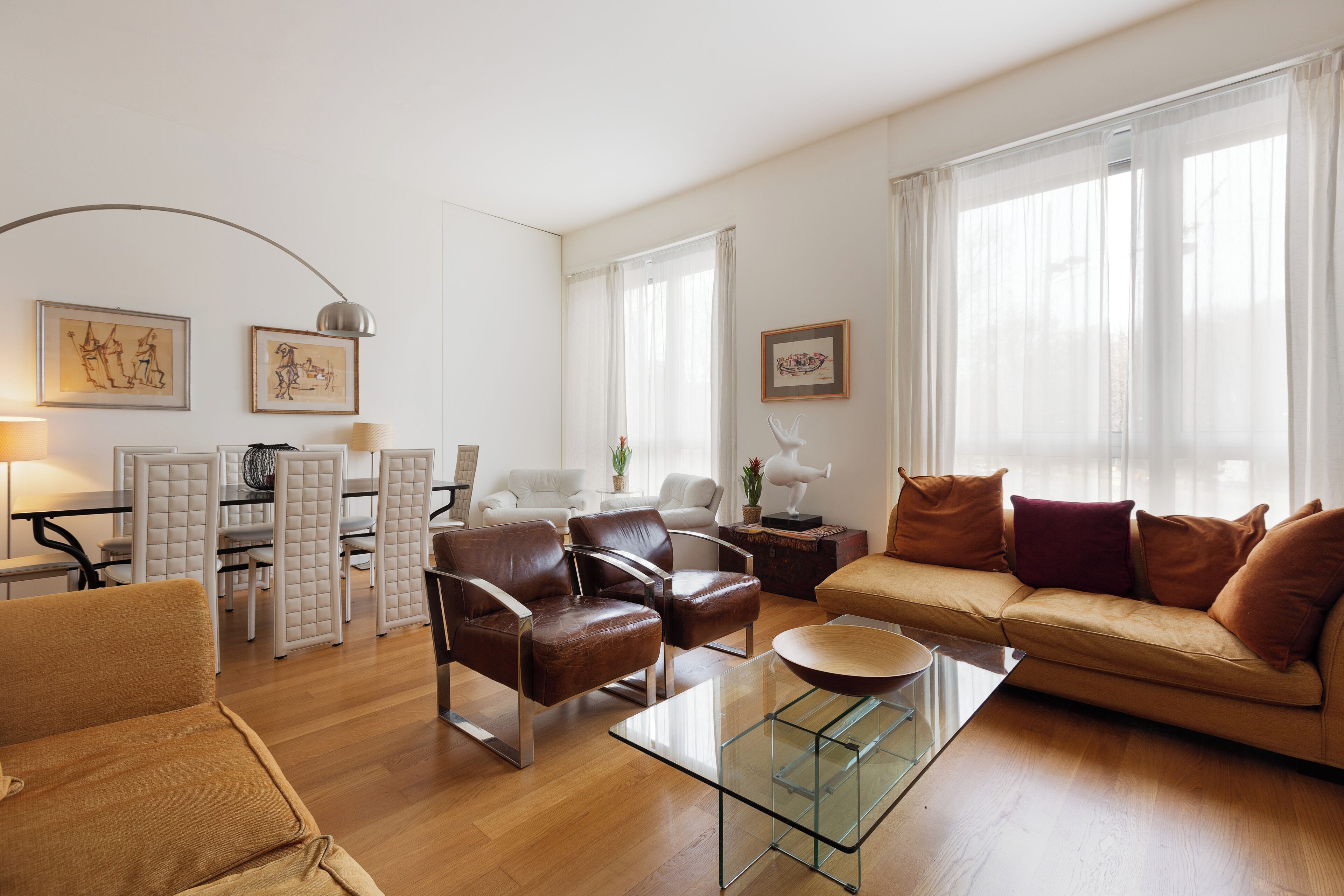 Ein modernes Wohnzimmer mit einer Couch, Sesseln, einem Glastisch und einem Essbereich mit Tisch und Stühlen.