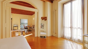 A hotel room with a wooden floor, a bed, a dining area with chairs and a table, and a large window with curtains. - Brera Apartments in Arena (Milan)