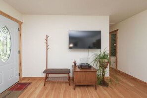 A room with a wooden bench, a small wooden table with a record player, a potted plant, and a flat-screen TV mounted on the wall. - Sycamore Shade: 151 House, HOT TUB, Mountain Views (Afton)