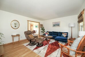 A living room with a brown leather chair, a blue sofa, and a red and white rug. There is a wooden coffee table, a small side table, and a lamp. - Sycamore Shade: 151 House, HOT TUB, Mountain Views (Afton)