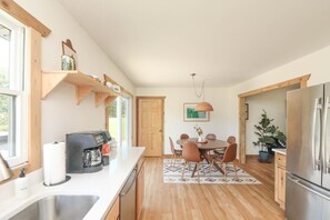A modern kitchen with wooden shelves, a coffee maker, a dining table with chairs, and a refrigerator.