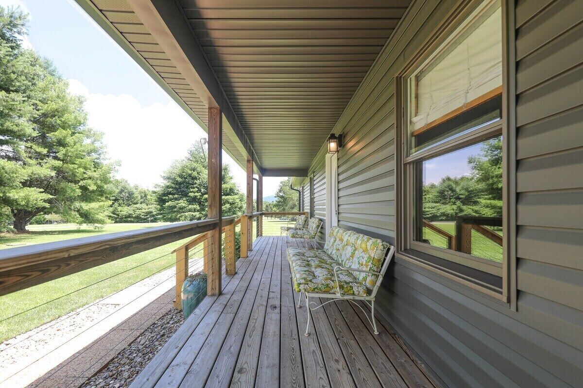 A covered porch with a wooden deck, a bench, and a view of a green landscape.
