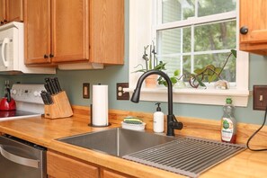 A kitchen with wooden cabinets, a stainless steel sink, a window with plants, and a red kettle. - Blue Rivers Cottage with Mountain Views (Afton)