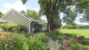 A green house with a porch, surrounded by a garden with various plants and flowers. - Blue Rivers Cottage with Mountain Views (Afton)