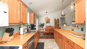 A kitchen with wooden cabinets, a dining area with chairs, and a coffee maker. - Blue Rivers Cottage with Mountain Views (Afton)