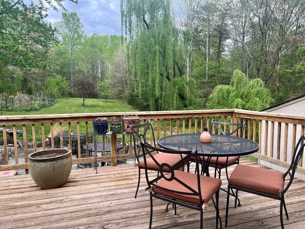 A wooden deck with a round table and chairs, surrounded by a wooden railing. - Blue Rivers Cottage with Mountain Views (Afton)