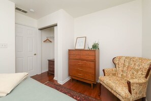 Une chambre à coucher comprenant un lit, une commode, une chaise et une porte donnant sur une autre pièce.