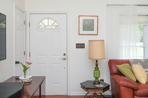 A living room with a white door, a green table lamp, a leather sofa with cushions, and a framed picture on the wall. - Blue Rivers Cottage with Mountain Views (Afton)